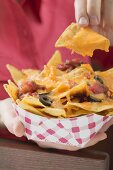 Woman holding nachos with melted cheese in cardboard container