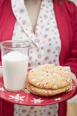 Frau hält Teller mit Weihnachtscookies und Glas Milch