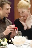 Man giving woman diamond ring over romantic meal