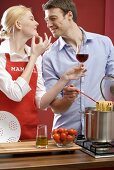 Couple cooking spaghetti & tomatoes, woman holding glass of wine