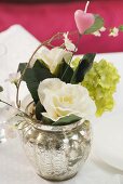 Blumenstrauss mit rosa Herz in Silbervase auf gedecktem Tisch