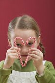 Small girl looking through heart made from two candy canes