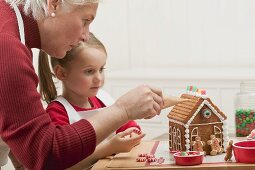 Small girl and grandmother decorating gingerbread house
