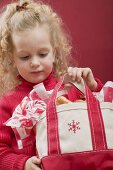 Kleines Mädchen hält Tasche mit Zuckerstangen und Plätzchen