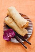 Spring rolls with orchid and chopsticks on plate