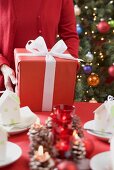 Woman putting Christmas parcel on laid table