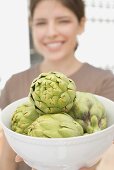 Young woman holding bowl of fresh artichokes