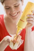 Young woman putting mustard on hot dog