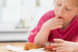 Little girl eating chicken nuggets with ketchup