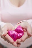 Woman holding heart-shaped chocolates in pink foil