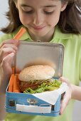 Girl holding lunch box containing burger & carrots