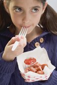 Little girl eating frankfurters with ketchup