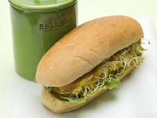A hot dog with sprouts beside a ceramic pot