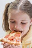 Mädchen beisst in ein Stück Salamipizza