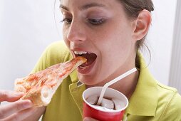 Woman holding cola & biting into slice of pizza Margherita