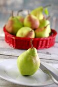 A pear on a plate in front of a basket of pears