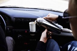 Pouring coffee out of thermos in a car into a cup