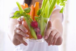 Girl holding a bowl of vegetable sticks with radishes