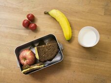 Lunchbox mit Pausenbrot, Obst und ein Glas Milch