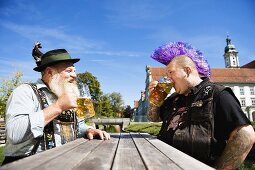 Man with Mohawk hairstyle & man in Bavarian dress in beer garden