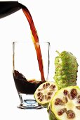 Pouring Noni juice into glass, fresh fruits aside