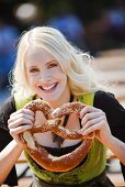 Germany, Bavaria, Munich, English Garden, Young woman holding soft pretzel, close-up