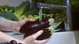 Washing aubergines under running water