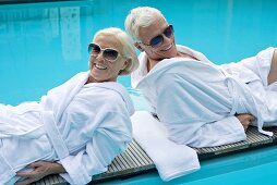 Älteres Paar in Bademänteln auf Holzliege am Swimmingpool