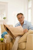 Mature man reading newspaper on sofa