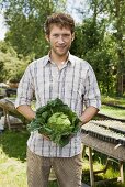 Young man holding savoy cabbage in market garden (outdoors)