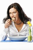 Young woman eating bowl of spaghetti with fork, portrait