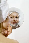 Young woman applying face mask looking into mirror smiling