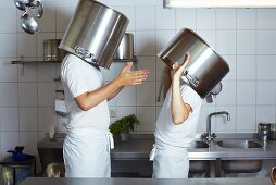 Two chefs having discussion with large pans on their heads