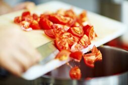 Koch kippt geschnittene Tomaten in Kochtopf