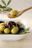 Green and black olives in small dish and on wooden spoon