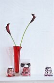 Roter Glaskrug mit zwei blutroten Callas, drei ungedrehte Gläser