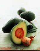 Halbe Avocado mit Kern, im Hintergrund ganze Früchte