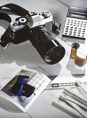 Fotokamera liegt neben Taschenrechner auf weiß-gestrichenen Tisch