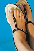 Füße einer Frau mit golden lackierten Zehennägeln in Sandalen