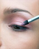 Extreme close-up of woman's eye while applying pink eye shadow
