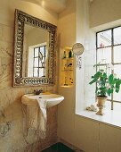 Über d. Waschbecken hängt ein Spiegel mit verziertem Goldrahmen