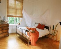 Eisenbett mit Moskitonetz dient als Himmelbett(orangefarb. Decke)