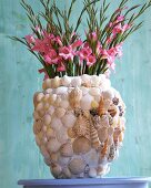 Bauchige Tonvase mit Muscheln u. Schnecken beklebt, enthält Gladiolen