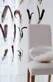 Feather in pocket of transparent curtain and plastic cushion on white chair