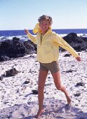 Frau läuft barfuß am Strand, gelbe Jacke, Shorts