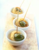 Three bowls of green olives with pastry crust on skewers