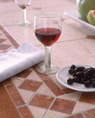Glas Rotwein und ein Teller mit schwarzen Oliven
