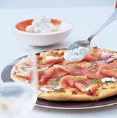 Auf eine Pizza mit Räucherlachs kommt ein Löffel Dillcreme