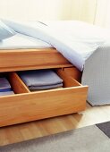 Folded bed sheets in open wooden drawer under bed
