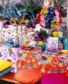 Table laid colourfully with floral table cloth, cushions and round flower lamp